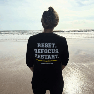 Person wearing Reset Refocus Restart Shirt on Beach Athlete Mindfulness